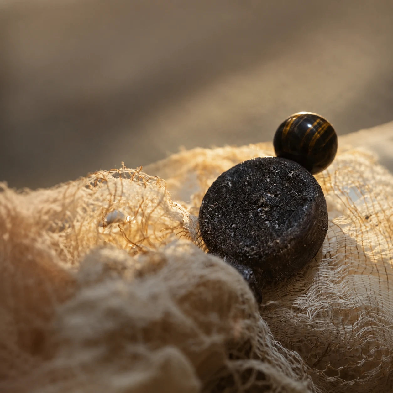 Black sculptural fragrance bottle on woven textile